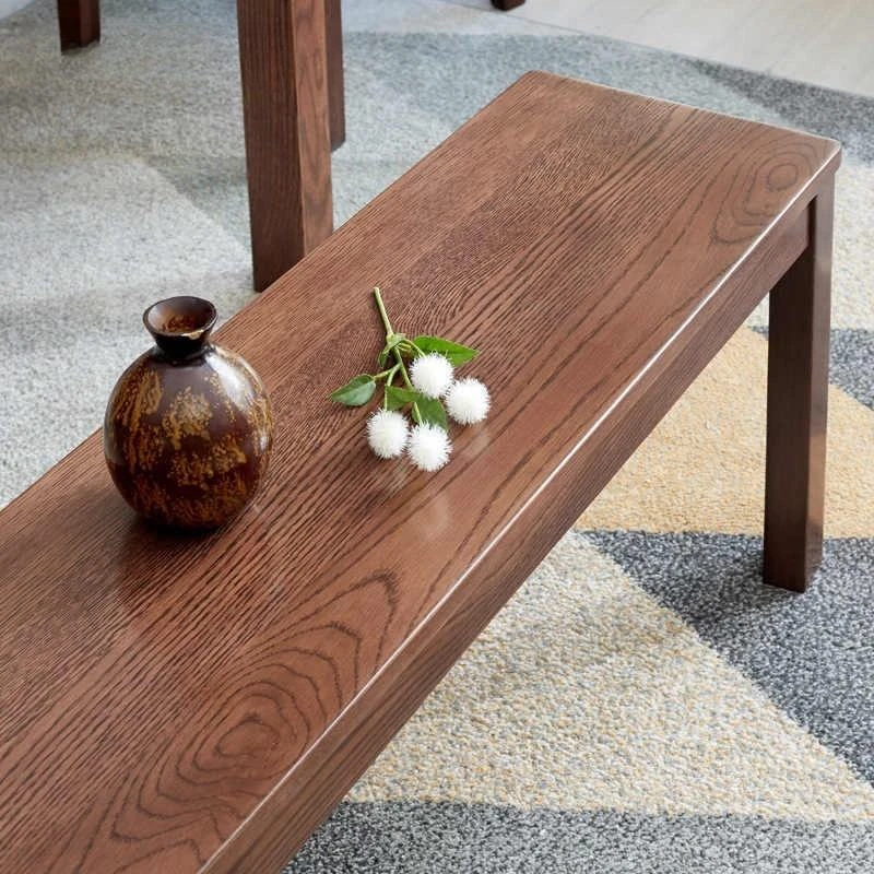 manna-oak-dining-bench-material-detail-cd1003 Close-up of the reddish brown oak bench seat showing the oak grain pattern and a small ceramic vase.