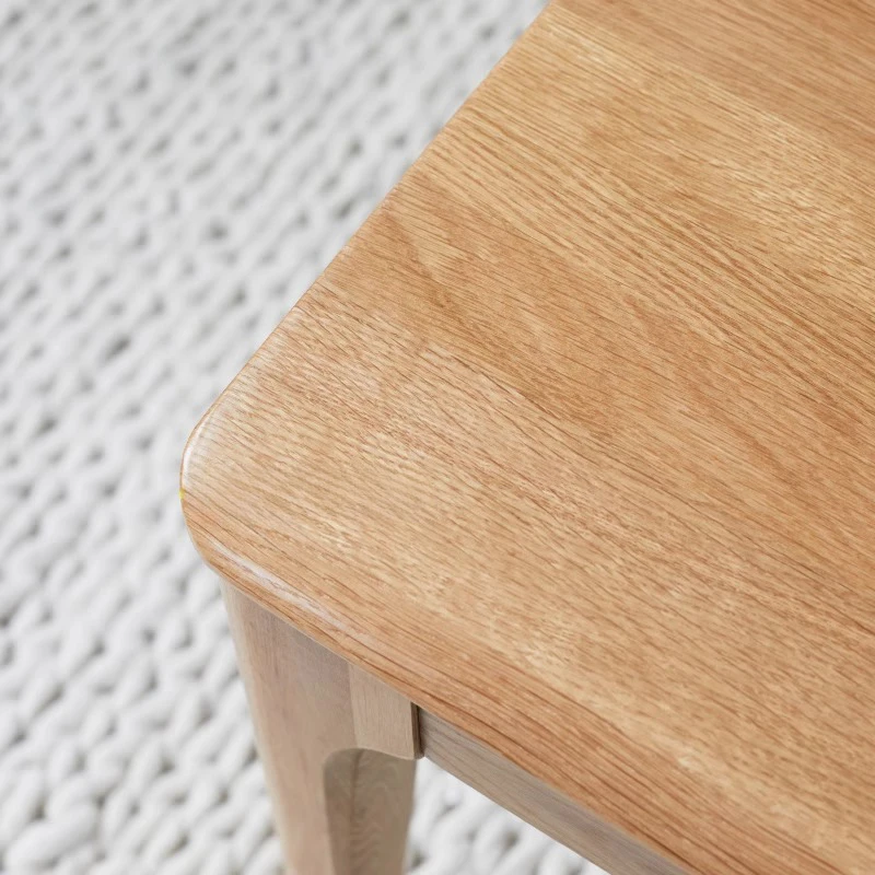 manna-oak-dining-bench-material-detail-cd1004 Close-up of a solid oak bench top showing the rounded corner and natural light oak grain beside a woven rug.