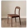 Front view of an oak dining chair with a rounded open backrest and contoured solid wood seat on a pale wood floor.