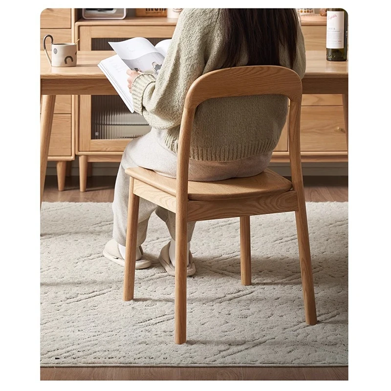 Lifestyle view of a person reading while seated on an oak dining chair with a curved backrest at a wooden table.