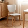Lifestyle view of an oak dining chair with a white upholstered seat and backrest beside an oak chest of drawers.