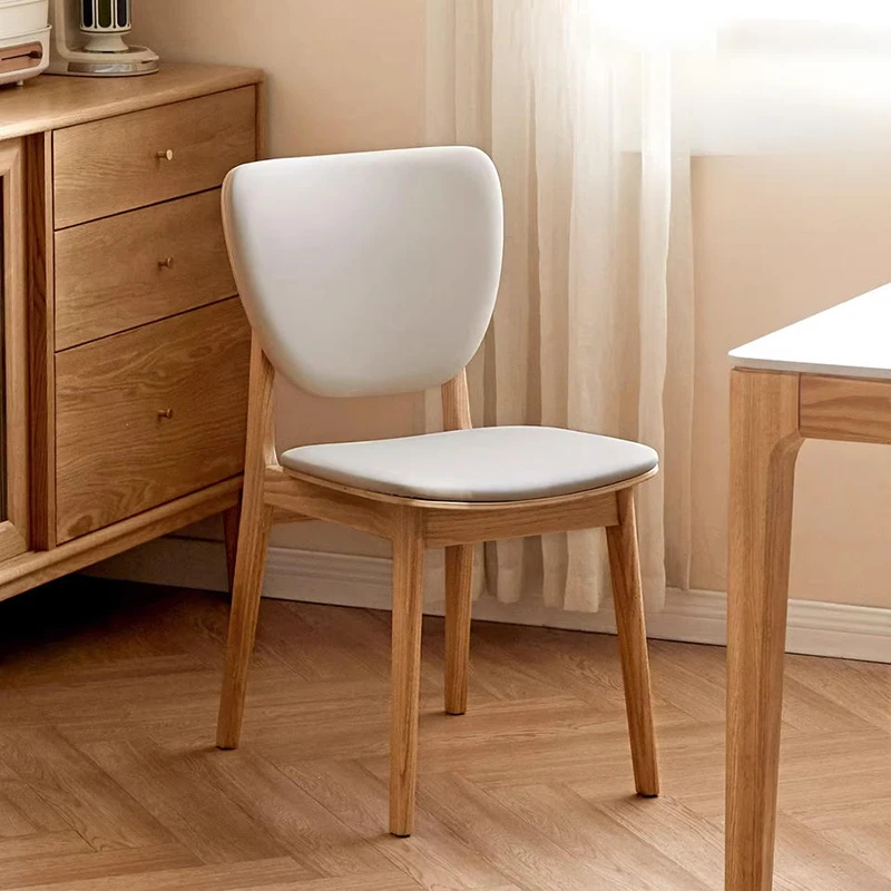 Lifestyle view of an oak dining chair with a white upholstered seat and backrest beside an oak chest of drawers.