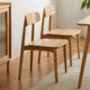 Lifestyle view of two oak dining chairs with curved wooden backrests beside a walnut table in a bright dining room.