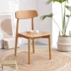 manna-oak-dining-chair-living-room-cy1019 Solid oak dining chair with a curved backrest placed in a minimalist living room on a round jute rug beside a plant.