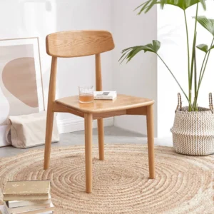 manna-oak-dining-chair-living-room-cy1019 Solid oak dining chair with a curved backrest placed in a minimalist living room on a round jute rug beside a plant.