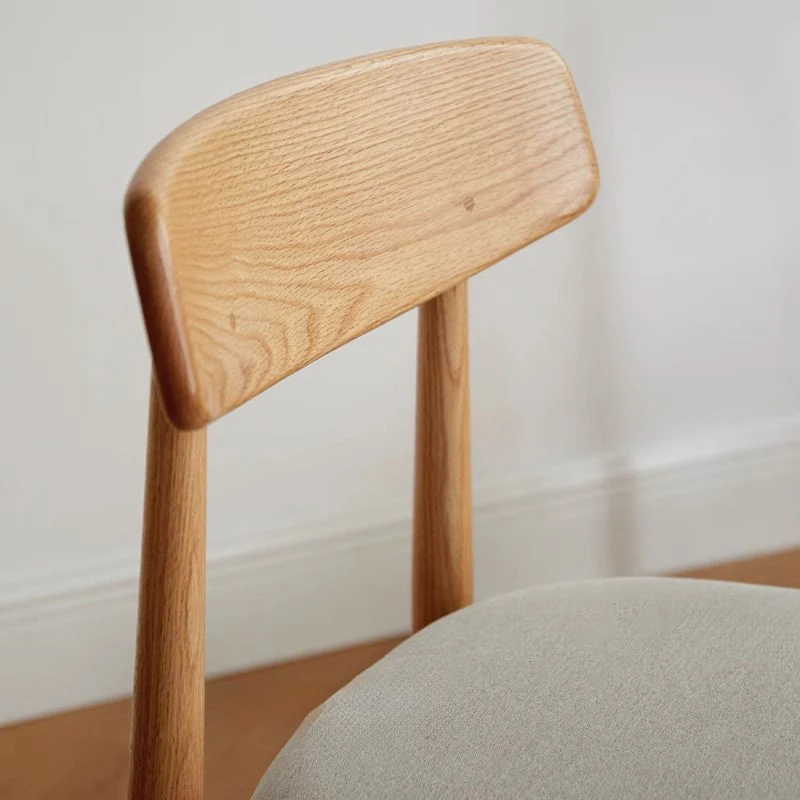 Material detail view of an oak dining chair backrest showing natural wood grain above a grey fabric seat.