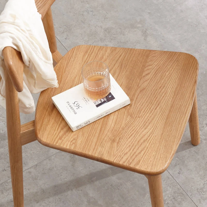 manna-oak-dining-chair-seat-detail Detail close-up of the oak dining chair seat showing natural wood grain with a glass and book resting on it.