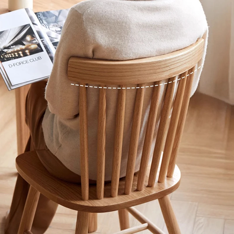 Back view of oak spindle back dining chair with a person and folded jacket resting over the curved crest rail.