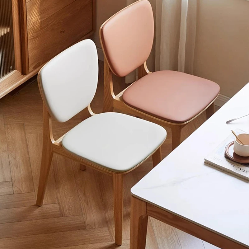 Two oak dining chairs with rounded upholstered backs shown in white and pink upholstery on herringbone flooring.