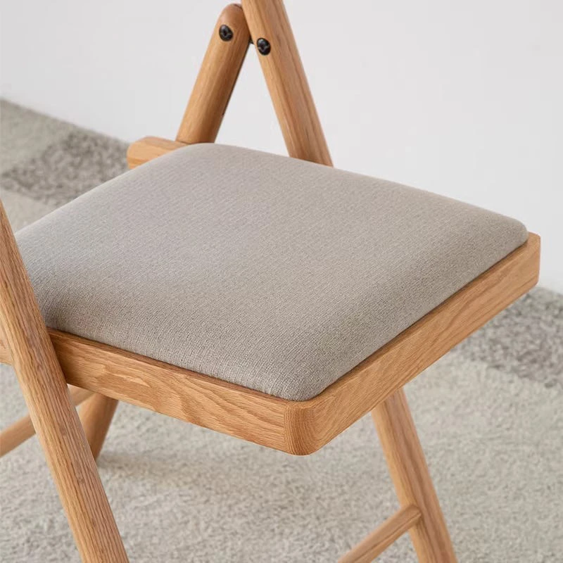 Close-up detail of the light oak folding chair seat showing the grey padded cushion and black folding hinge hardware.