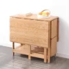 Lifestyle scene of an oak folding dining table with both hinged leaves dropped into a compact sideboard shape.