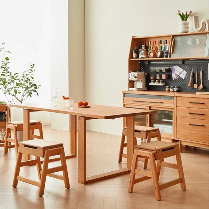 Lifestyle view of oak folding step stools with hinged seats and storage placed around a wooden dining table in a kitchen.