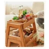 Detail view of oak folding step stool opened into a two tier storage side table holding bottles and snack baskets.
