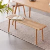 manna-oak-rattan-dining-bench-lifestyle Lifestyle view of a natural oak dining bench with a woven rattan cane seat and tapered round legs beneath a dining table.