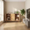 Front view of a solid oak sideboard with folding doors, three central drawers with wood knobs and brass capped tapered legs beside a window.