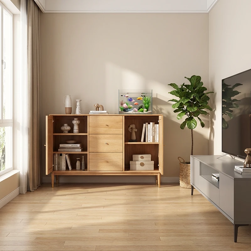 Front view of a solid oak sideboard with folding doors, three central drawers with wood knobs and brass capped tapered legs beside a window.