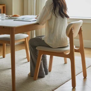 Lifestyle view of a person seated on a grey upholstered oak dining chair at a white stone topped table.