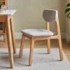 manna-oak-upholstered-dining-chair-side-view Side view of an oak dining chair with a light grey upholstered seat and curved padded backrest in a dining room.
