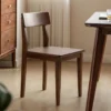 manna-walnut-dining-chair-curved-back-main Full view of a solid walnut dining chair with a curved backrest and contoured wooden seat in a bright dining room.