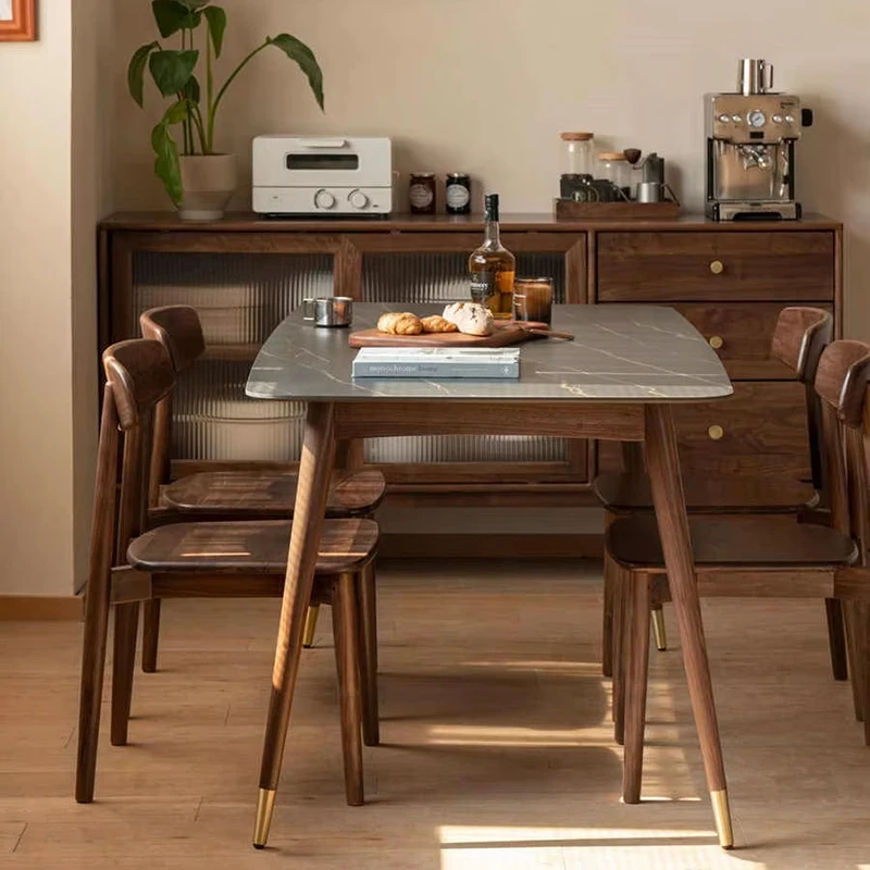 Lifestyle view of two solid walnut dining chairs with curved backrests set at a grey marble dining table in a warm dining room.