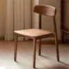 Front view of a solid walnut dining chair with a curved open backrest and tapered legs standing on oak flooring.