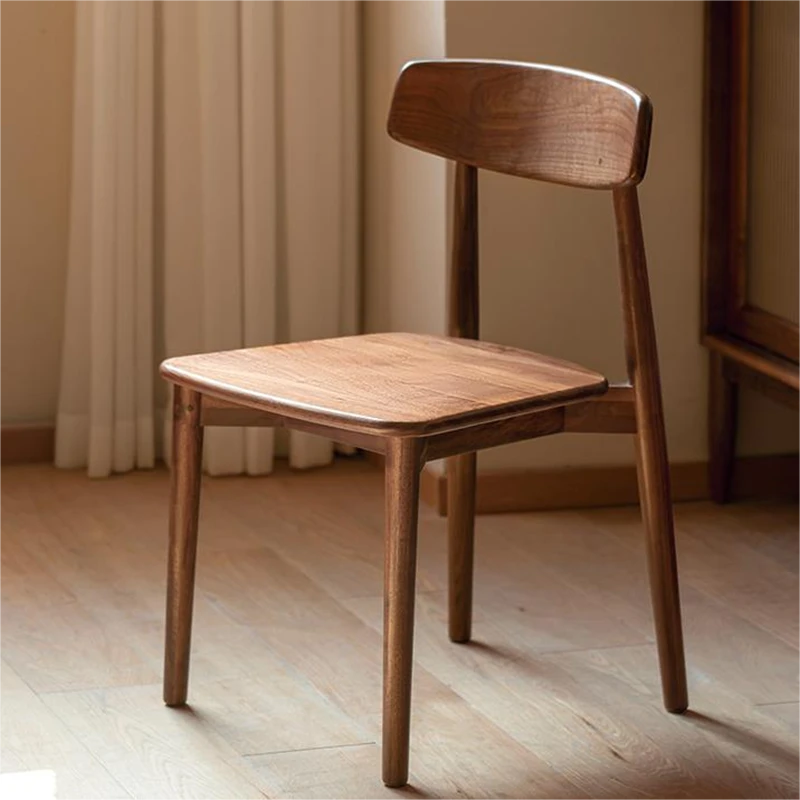 Front view of a solid walnut dining chair with a curved open backrest and tapered legs standing on oak flooring.