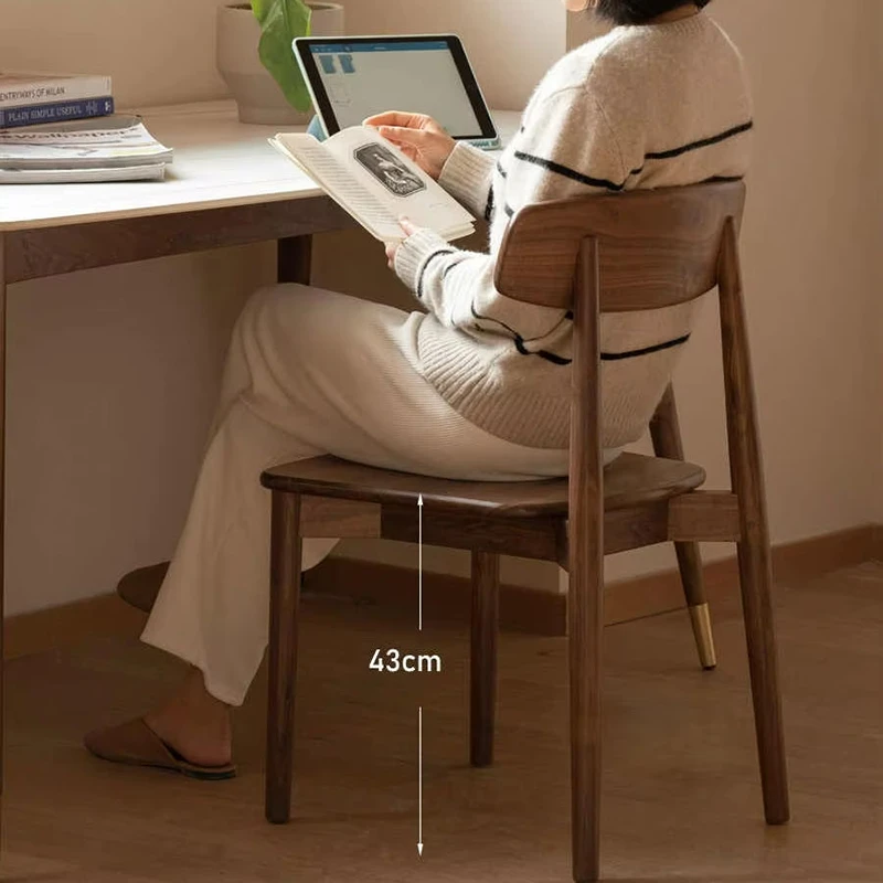 Side view of a woman reading at a wooden desk while seated on a solid walnut dining chair with a 43cm seat height marker.