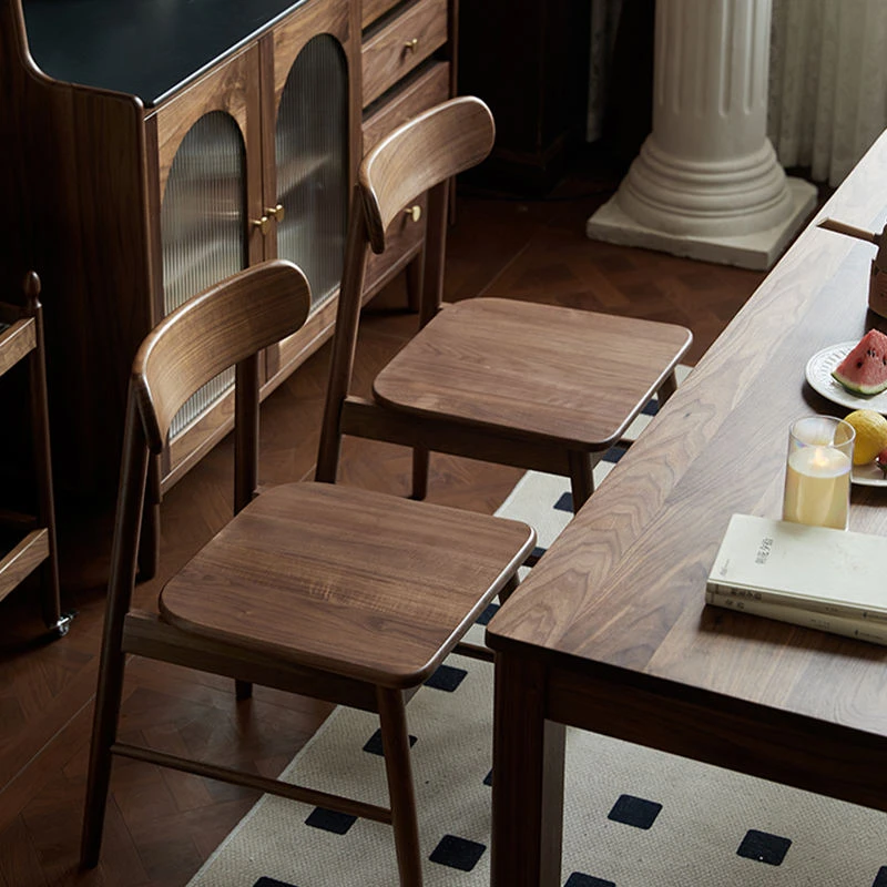 Lifestyle view of two walnut dining chairs with wooden seats pulled up to a walnut dining table in a warm living space.