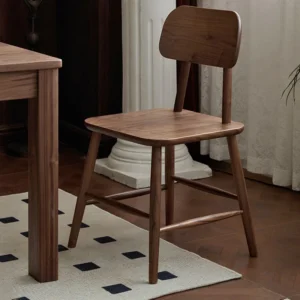 Solid walnut dining chair with a curved backrest and cross stretchers placed beside a table on a patterned rug.