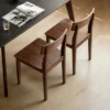 manna-walnut-dining-chair-pair-lifestyle High angle view of two solid walnut dining chairs with curved backrests beside a black marble dining table.