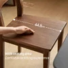 manna-walnut-dining-chair-wide-seat-detail Detail close-up of a hand resting on the solid walnut dining chair seat with a 44.8cm width dimension overlay.