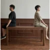 manna-walnut-rectangular-dining-table-strength-test Strength test image showing two people sitting on a solid walnut dining table against dark wood panelling.