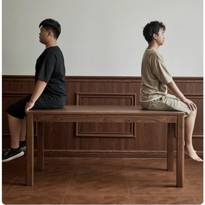 manna-walnut-rectangular-dining-table-strength-test Strength test image showing two people sitting on a solid walnut dining table against dark wood panelling.