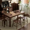 manna-walnut-rectangular-dining-table-with-stools-lifestyle Lifestyle scene of a rectangular walnut dining table with four wood chairs and a round stool in a vintage room.