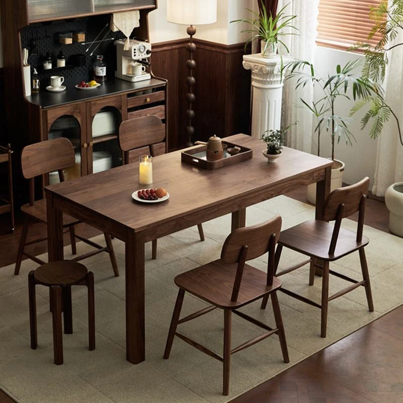 Lifestyle scene of a rectangular walnut dining table with four wood chairs and a round stool in a vintage room.