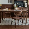 manna-walnut-rectangular-dining-table-wood-grain-detail Front view of a solid walnut dining table with straight block legs styled with wood chairs and a stool on a dotted rug.