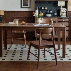Front view of a solid walnut dining table with straight block legs styled with wood chairs and a stool on a dotted rug.