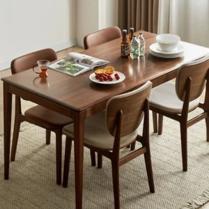 Lifestyle scene of a walnut dining table set with drinks and fruit, surrounded by wood and leather chairs on a rug.