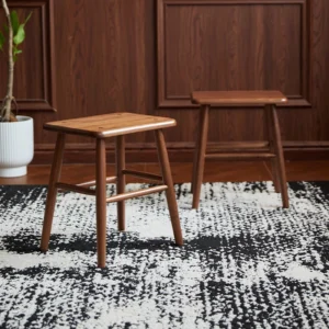 manna-walnut-square-stool-lifestyle Two solid walnut square wooden stools with splayed legs and cross stretchers standing on a patterned rug.
