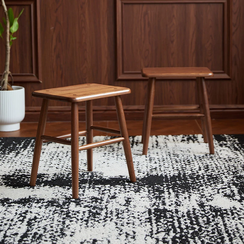 manna-walnut-square-stool-lifestyle Two solid walnut square wooden stools with splayed legs and cross stretchers standing on a patterned rug.