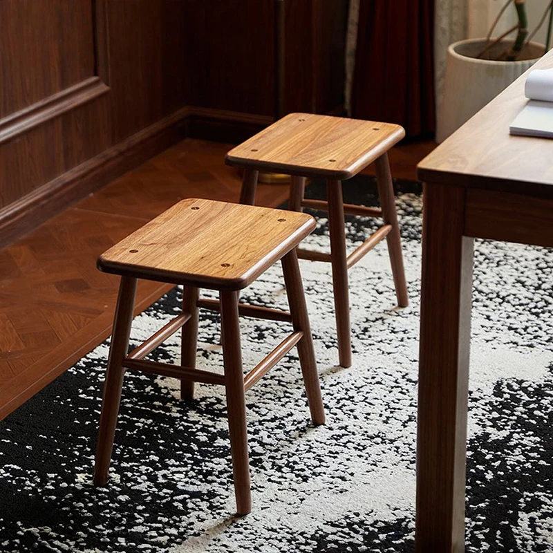 manna-walnut-square-stool-pair-lifestyle High angle view of two solid walnut square stools with rounded seats and angled legs on a black and white rug.