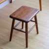manna-walnut-square-stool-seated-detail Close-up detail of a dark walnut square stool top showing figured wood grain and four wooden screw plugs.