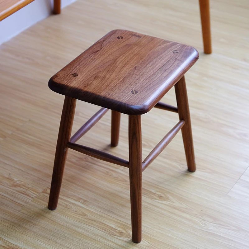 manna-walnut-square-stool-seated-detail Close-up detail of a dark walnut square stool top showing figured wood grain and four wooden screw plugs.