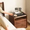 Black walnut nightstand with a black glass top beside a bed in a warm scene