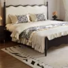 Cream upholstered bed frame with black wood posts and wavy headboard front view