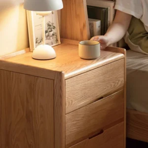 Natural oak 3 drawer nightstand beside bed in a bright bedroom