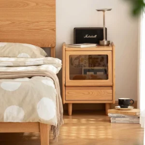 oak-nightstand-glass-door-drawer-bedroom-scene Oak nightstand with glass door and drawer beside a bed in a bright bedroom scene